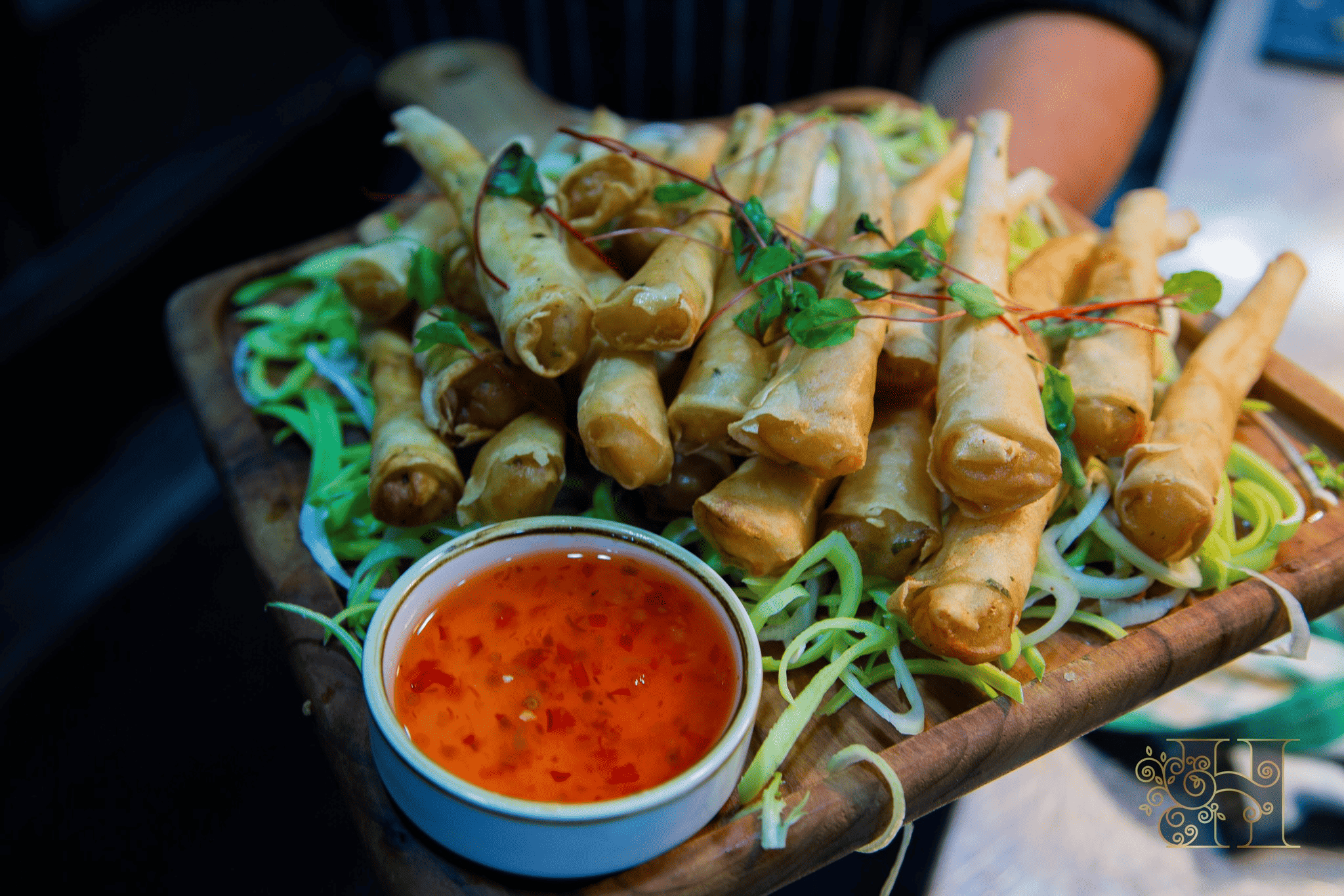Crispy spring rolls with fresh garnish and tangy dip on a wooden platter at an Indian wedding event.