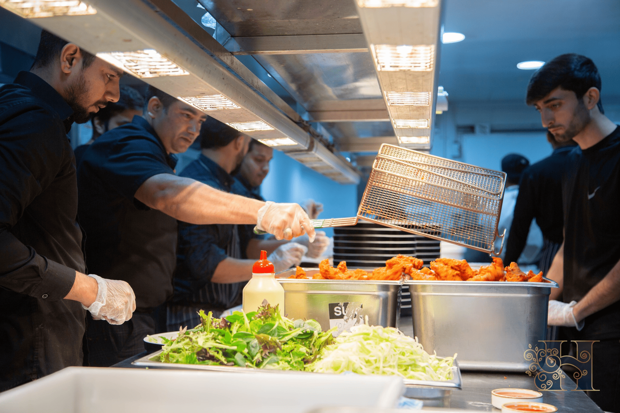 Catering staff serving spicy chicken with fresh salad in a kitchen.